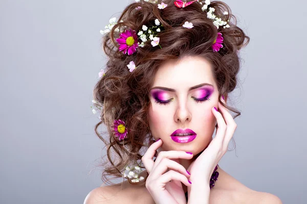 Jeune belle femme avec des fleurs dans ses cheveux et un maquillage lumineux — Photo