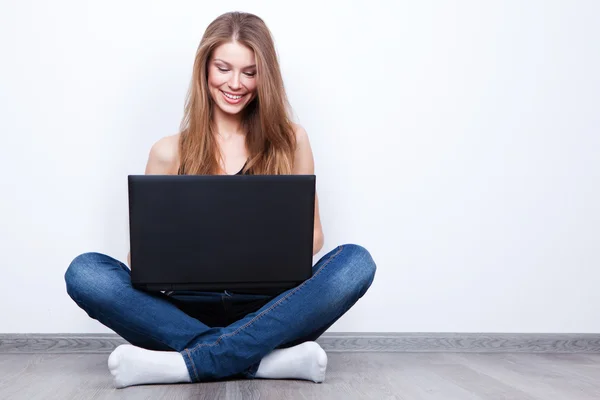 Bella giovane donna seduta sul pavimento con computer portatile Immagine Stock