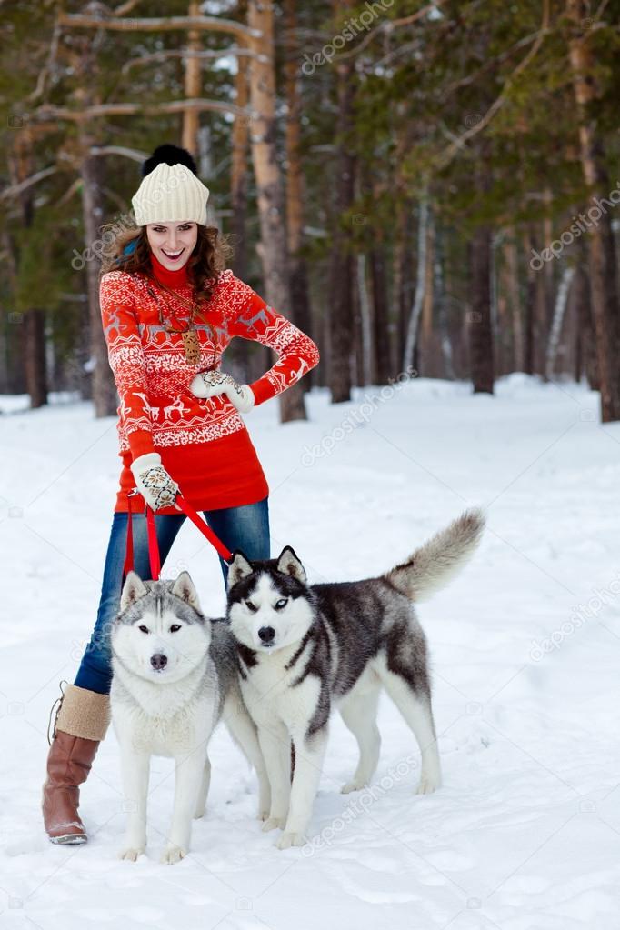 Happy woman playing with siberian husky dogs in winter forest