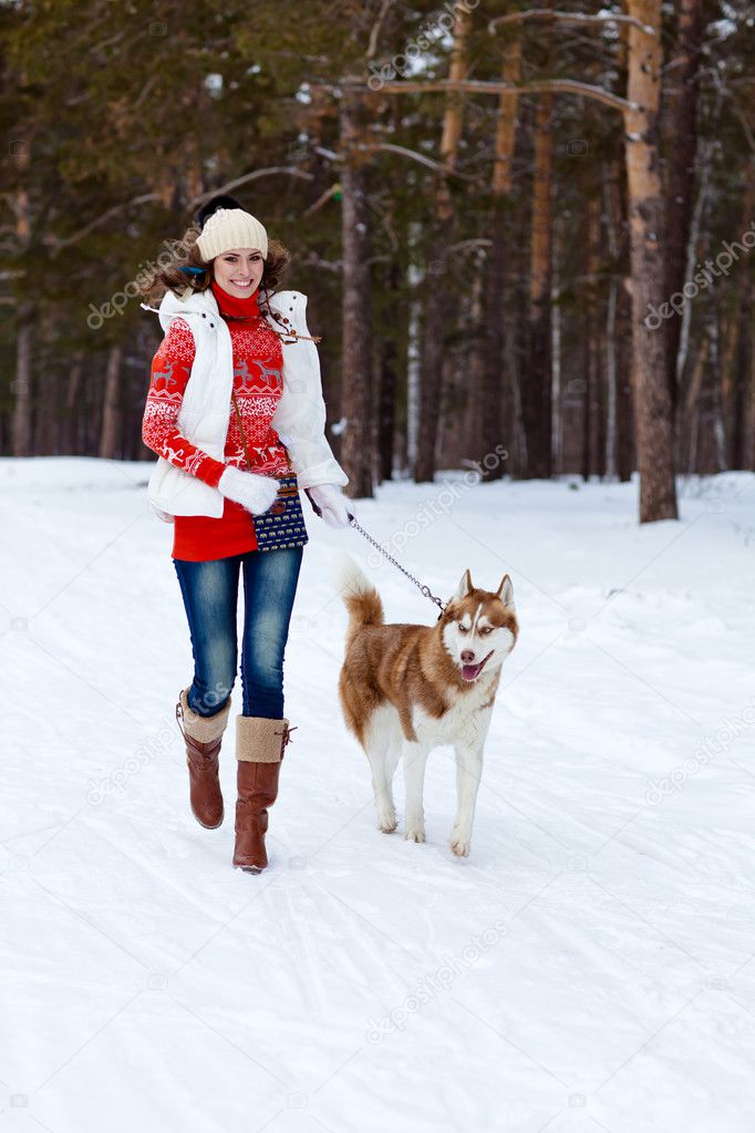 Happy woman playing with siberian husky dog in winter forest