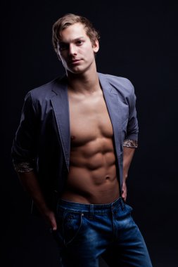 szexi macsó fiatalember nyitott kabát alatt sötét háttér