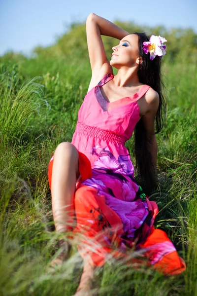 Außenporträt einer jungen schönen Frau in rotem Kleid und Blume im Haar — Stockfoto