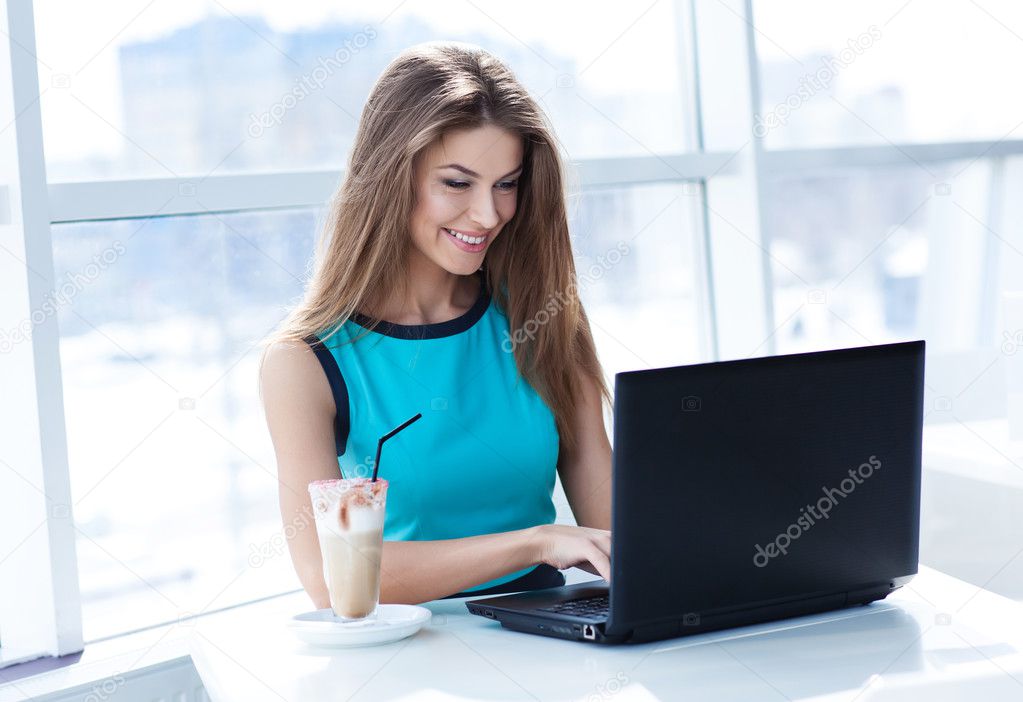 Portrait of beautiful smiling woman sitting in a cafe with laptop