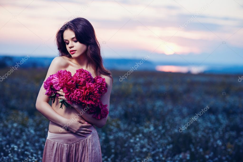 Beautiful young woman posing in the sunset field with flowers