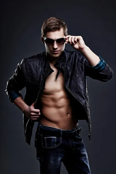 Young handsome macho man in sunglasses with open leather jacket — Stock Photo, Image