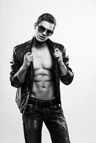 Jeune homme macho beau en lunettes de soleil avec veste en cuir ouverte — Photo