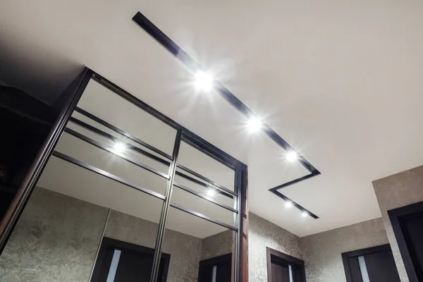 suspended ceiling with halogen spots lamps and drywall construction in empty room in apartment or house. Stretch ceiling white and complex shape.