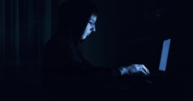 Gece karanlık odada bilgisayarın başında bilgisayar korsanı olarak çalışan kapüşonlu, tehlikeli bir genç adam görülüyor.