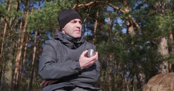 一个穿着暖和衣服的男人在松林里 拿着杯子 紧张地说些什么 拍了拍他的手指 — 图库视频影像