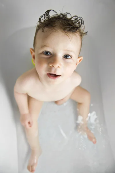 Cute baby boy with funny hair bath in the bathtub looking at the — Stock Photo, Image