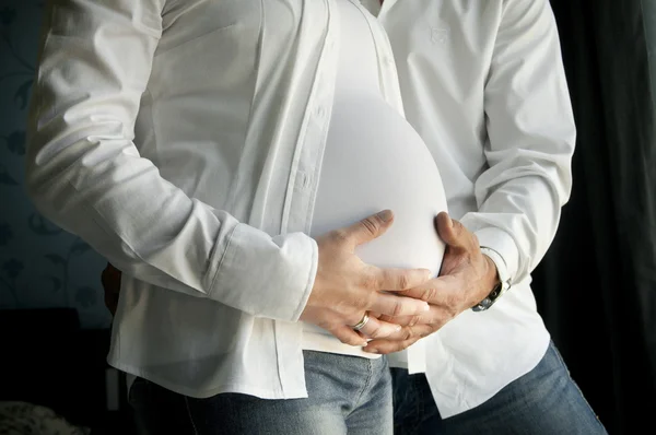 Man and woman's hands over pregnant belly on black in white shir