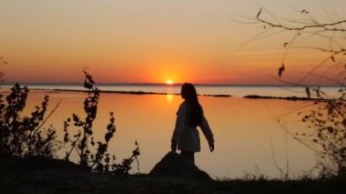 Kumsalda yürüyen bir kadın sonbahar günbatımını seyrediyor.