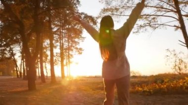 Gün batımını, sonbahar çam ormanını ve zevk için kollarını açmış yürüyen bir kızı resmediyor.