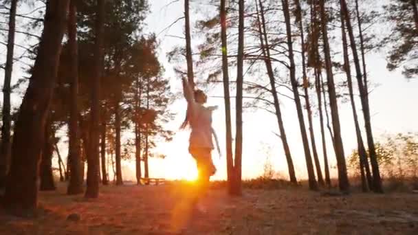 Młoda uśmiechnięta kobieta skacze z radości w sosnowym lesie o zachodzie słońca — Wideo stockowe