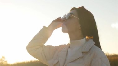 Gözlüklü genç bir kadın güneş ışınlarına ve gülüşlere bakıyor.