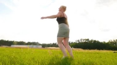 Güzel sarışın yeşil alanda dönüyor ve gülüyor.