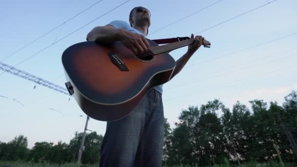 Güneş gözlüğü takan ve şapkalı erkek müzisyen aşağıdan gitar görüntüsü çalıyor. — Stok video
