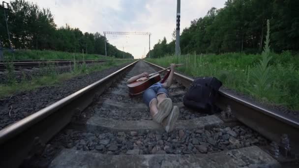 男人躺在铁路的卧铺上，两腿交叉，弹吉他 — 图库视频影像