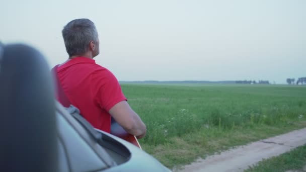 音楽家は壊れた車の近くの夏の間にフィールドでギターと歌を演奏する — ストック動画