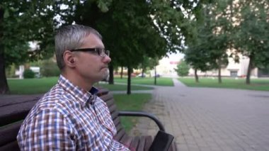 Adam kahve içiyor. Parkta kulaklıkla müzik dinliyor.