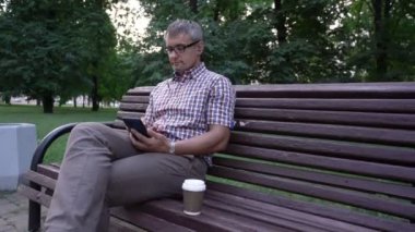 Adam sosyal medyayı kontrol ediyor ve parktaki kameraya bakıyor.