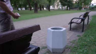 Adam parktaki çöp kutusuna boş kahve kağıdı atıyor.