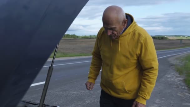 Seniorin steht auf Vorstadtstraße neben kaputtem Auto mit offener Motorhaube — Stockvideo