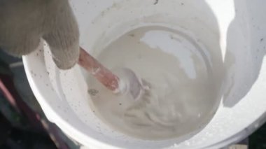 Elinde boya fırçası olan bir bahçıvan boya kabını boyayla karıştırıyor.