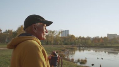 Olumlu yaşlı adam emekli sonbahar şehir parkının tadını çıkarıyor ve kahve molası veriyor.