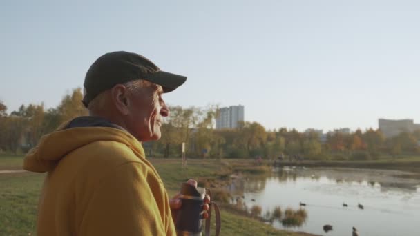O pensionista idoso positivo gosta do parque da cidade do outono e quebra a pausa com o café — Vídeo de Stock