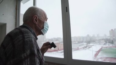 Yüz maskeli konsantre olmuş yaşlı adam dürbünle bakıyor.