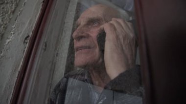 Gri saçlı endişeli yaşlı adam akıllı telefondan konuşuyor.