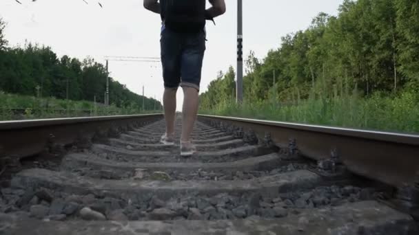 Viajero masculino camina con confianza con mochila sobre carriles de ferrocarril — Vídeos de Stock