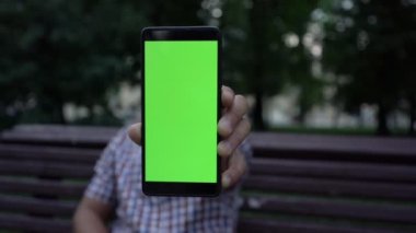 Adam yeşil ekranlı modern telefonu kamera lensine gösteriyor