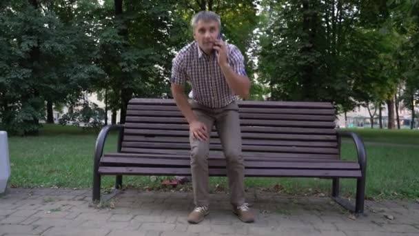 Homem sente dor nas costas levantando-se do banco falando no telefone — Vídeo de Stock