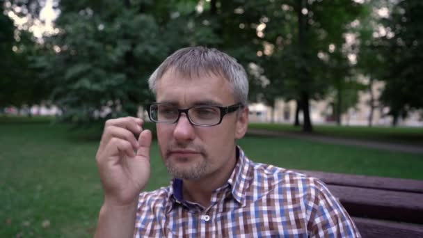 Az ember leveszi a szemüveg és dörzsöli a szemét fáradtan a parkban — Stock videók