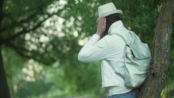 Lady bruna con cappello bianco e zaino si trova nel parco — Video Stock
