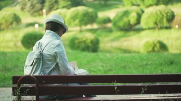 Lady μελαχρινή κάθεται στον πάγκο στο πράσινο πάρκο απολαμβάνοντας τη φύση — Αρχείο Βίντεο