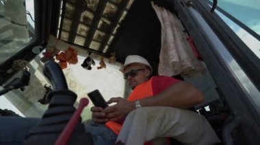 Kazıcı operatörü, kazı kabininde telefonla oynuyor