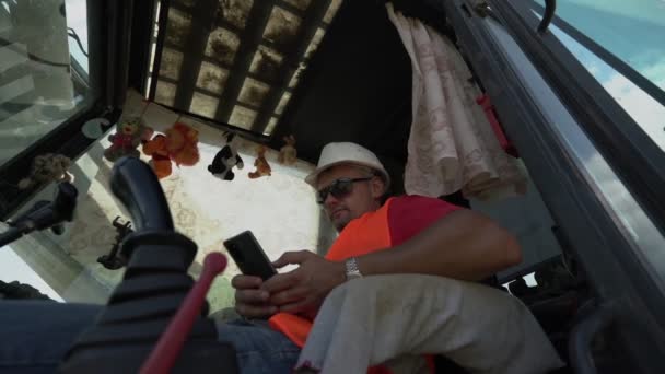 Graafmachine operator speelt in telefoon in graafmachine cabine — Stockvideo