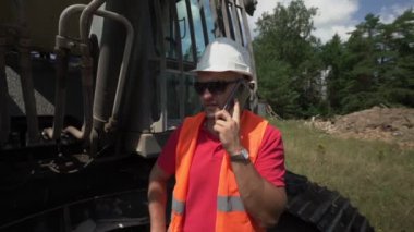 Adam sürüngen kazıcısının yanında duruyor ve telefonda konuşuyor.