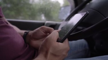 Modern akıllı telefonu elinde tutan adam araba kulübesinde oturuyor.