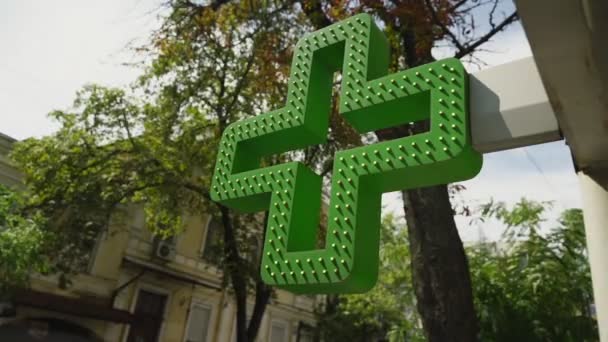 Grönt kors medicinsk symbol hängande över ingången till apotek byggnad — Stockvideo