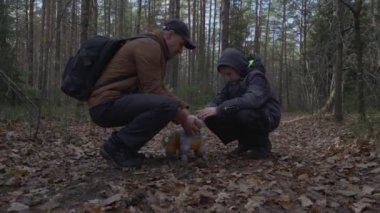 Baba ve oğul sonbahar orman yolunda çömelmiş bir köpeği okşuyor..