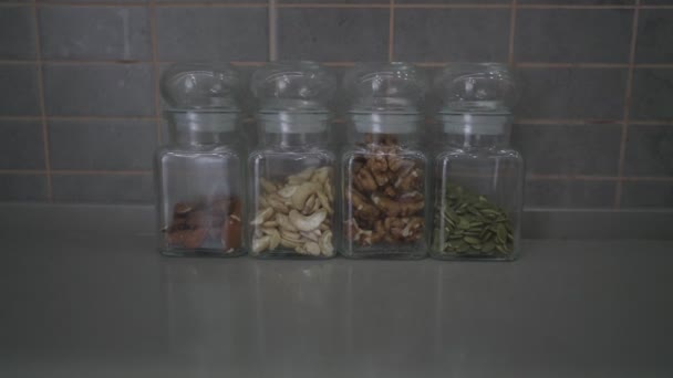 Raw nuts and seeds in glass jars standing in row on kitchen table — Stock Video