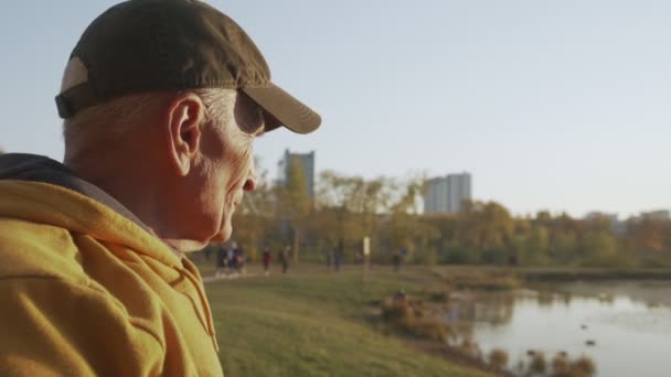 Sonbahar parkında şapkalı yalnız yaşlı büyükbaba duruyor. — Stok video