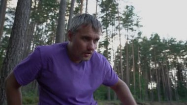 Oturan yorgun yetişkin adam, sıkı spor yaptıktan sonra alnından ter siler.