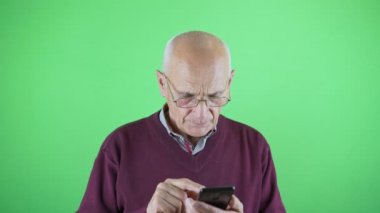 Gözlüklü yaşlı kişi daktilo numarası ve akıllı telefonuyla arıyor.