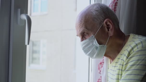 Hombre solitario con mascarilla médica mirando por la ventana — Vídeos de Stock