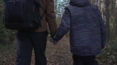Baba ve oğul turist çantasıyla orman yolunda el ele yürüyorlar..